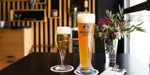 Zwei frisch gezapfte Biere mit Schaumkrone, ein Fürstenberg- und ein Paulaner-Weißbier, stehen auf Bierdeckeln neben einer Serviette mit "tom's"-Schriftzug.